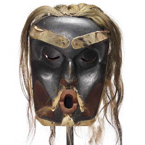 Dague en bois et un masque Dzunuḱwa de chef profondément sculpté, noir avec des taches rouges, les cheveux clairs.