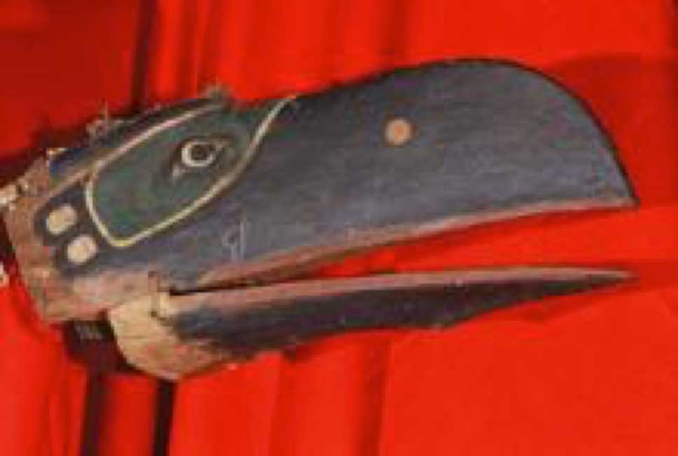 Photographie couleur un masque de Corbeau, Gwa’wina, en vue latérale, prise sur un fond rouge