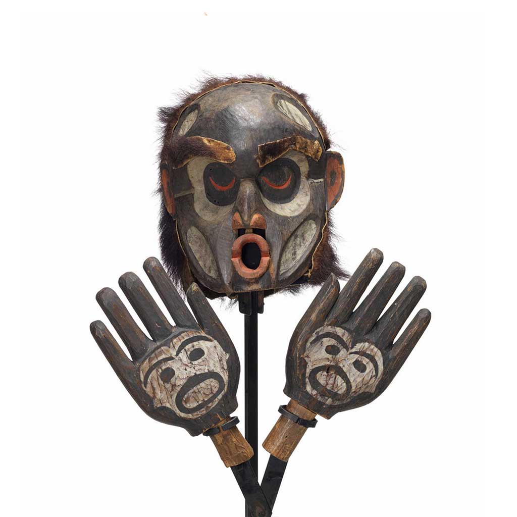 Un masque d'Ogresse Dzunuḱwa et d'une paire de mains sculptées, peints en noir avec des détails en blanc sur le visage et les mains, bouche rouge en cul de poule.