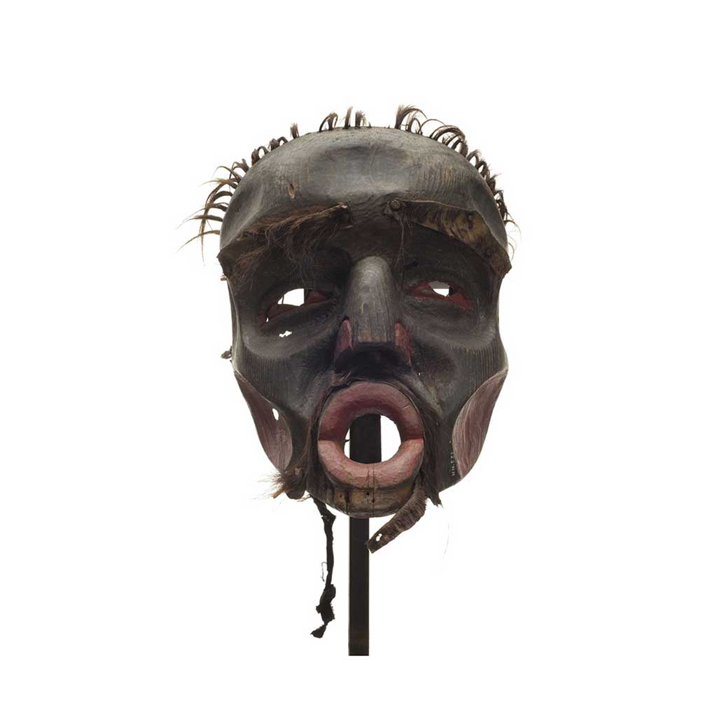 Un masque d'Ogresse Dzunuḱwa, peint en noir, du rouge foncé sur le nez, les joues, les pupilles et les narines, de courtes touffes de cheveux sur le crâne et de la fourrure usée.