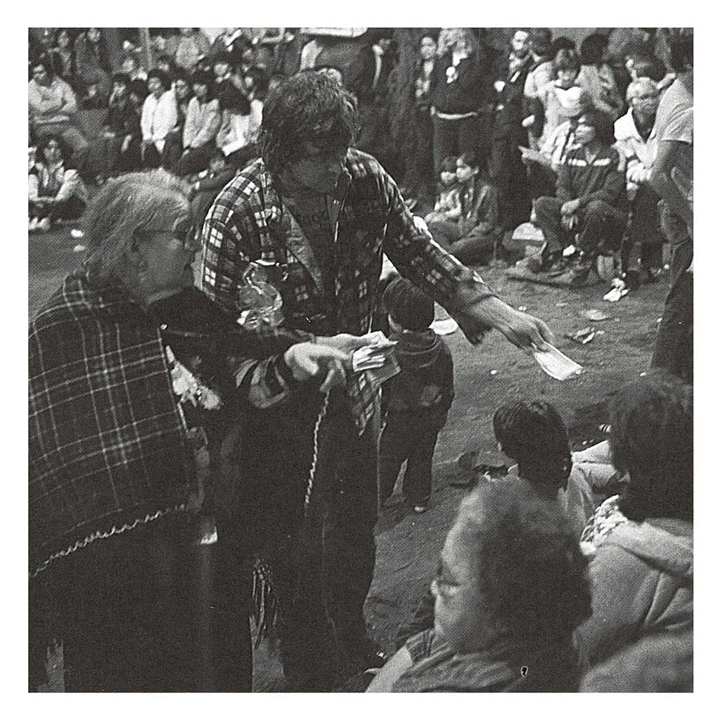 Black and white photograph shows a couple (presumed mother and son) handing out gifts of money at a potlatch.