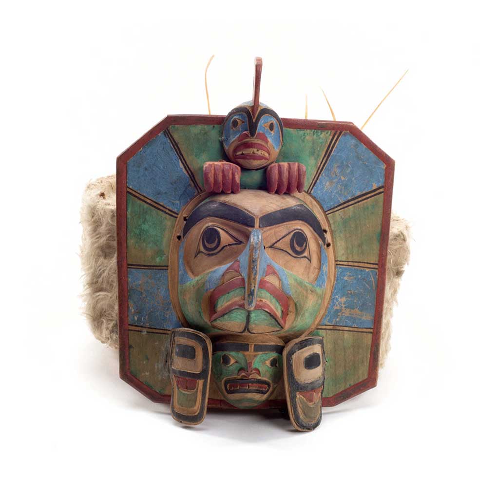Yaxwiwe' frontlet, carved wood hexagonal shape with blue and green sections, central bird face with whale figure above, ermine and sea lion whisker trim.