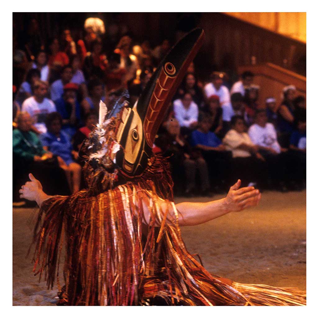 Photo couleur un danseur en attirail du cérémonial de l'écorce de cèdre rouge Tseka, lors un potlatch dans la maison cérémonielle.