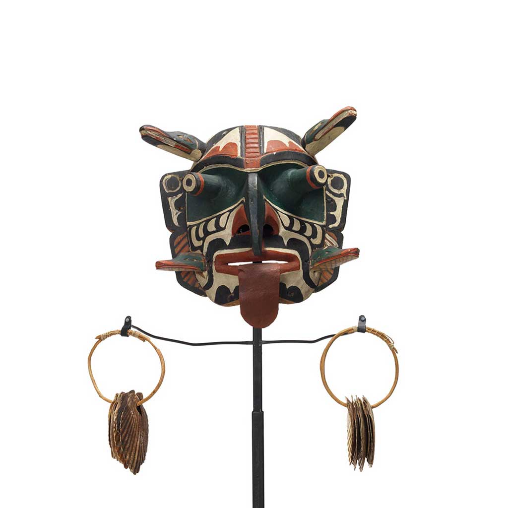 Xwixwi mask representing red snapper or cod, shown with sea shell rattles. Large protruding eyes, drooping tongue, 4 animal figures project from temples and cheeks.
