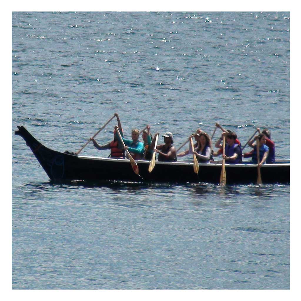 Colour photograph shows 20 paddlers in a Xwakwana or large tradition kwakwakw'wakw canoe.