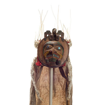 D'une coiffe circulaire de chefs Yaxwiwe', dents et yeux sertis d'ormeau, oiseau sculpté au sommet, traînée de tissu et d'hermine.