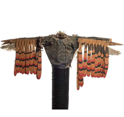 Un costume d'aigle des mers Kwigwis en veste en denim couverte de touffes de plumes cousues des rémiges en bois sculpté pendant des bras.