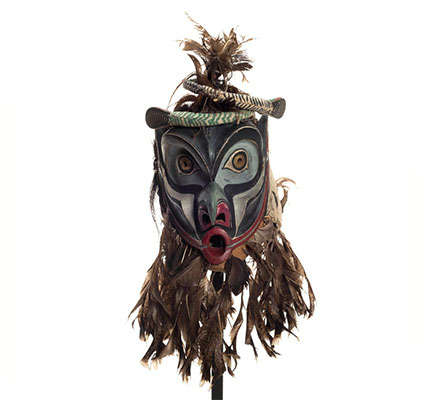 Bakwas mask with two coiled snakes atop highly arched eyebrows, brass disks with perforated centres for eyes, a beak-like nose, feather trim.