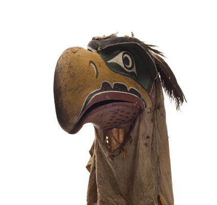 Un masque d'aigle Kwigwis, au bec jaune, l'orbite bleue, la bouche esquissée en rouge, un voile de coton noir.