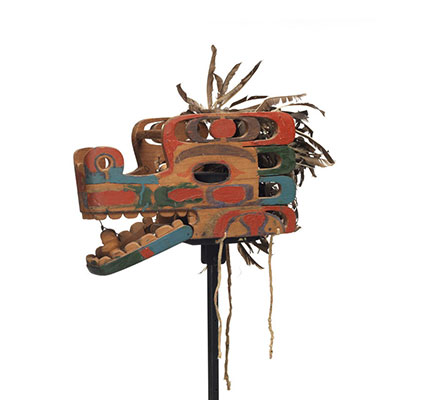Un masque de serpent Haietlik en planches clouées, à mâchoire articulée, de nombreux éléments découpés, des motifs bleu clair, vert et rouge, orné de plumes.