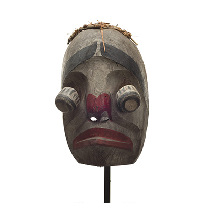 Un masque d'imitateur Atłakima, visage blanc, yeux globuleux articulés, lèvres et narines rouges, épais sourcils noirs, frange d'écorce de cèdre.