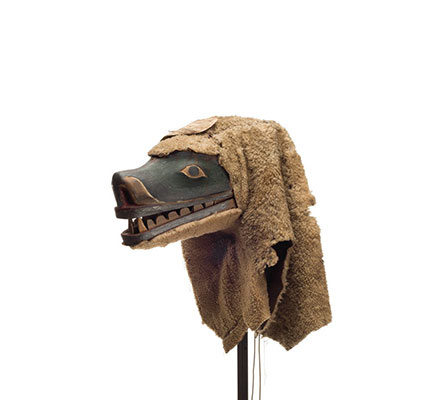 A Nanis or sea dog mask with long muzzle open mouth and sharp teeth, green paint surrounding eyes, sheep skin attached at back.