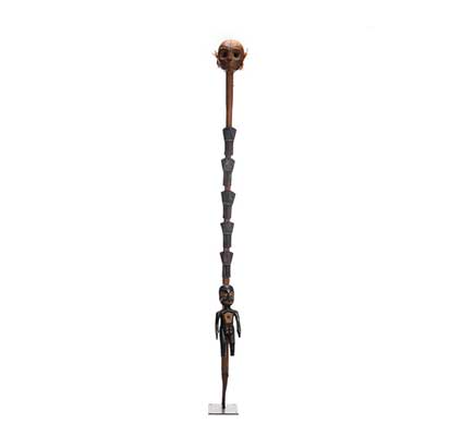 A carved, wooden staff with figure on the bottom, five coppers and a carved wooden skull at the top staff.