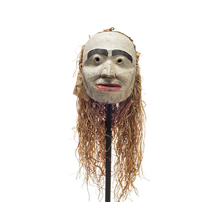 Forest spirit mask, humanoid features, mostly white face with red lips and prominent black eyebrows, cloth and cedar drape on back.