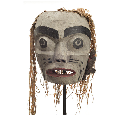 A large forest spirit mask, mostly white, red lips, large open mouth, some cedar trim on back and sides. Eyes are painted. Mask has no eyeholes.
