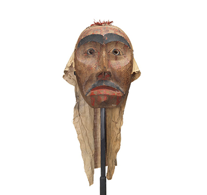 A mourning mask red cedar with painted black eyebrows pupils and moustache. Red paint drips on the forehead, below eyes and lips.
