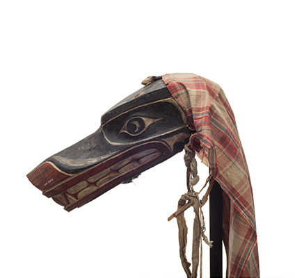 Un des masques de loup Xisiwe’, au long museau et aux grandes dents, peint en rouge et noir, avec des restes un voile de coton uni.