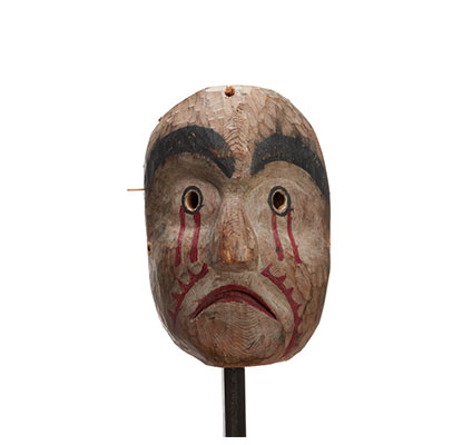 Un masque de deuil Kwasanuma, morne, en cèdre sculpté et peint, sourcils noirs, pupilles percées, du rouge coulant des yeux et sur les joues.