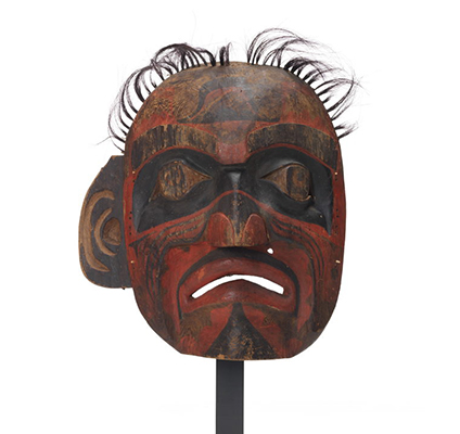 Large deaf man mask, lacks eyeholes, tufts of horsehair above, black bands of paint around eyes, mostly red and black markings on face, sad expression.