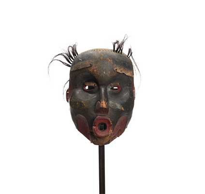 Un masque d'Ogresse Dzunukwa sculpté et peint en noir graphite, des lèvres en cul de poule et des touffes de cheveux.