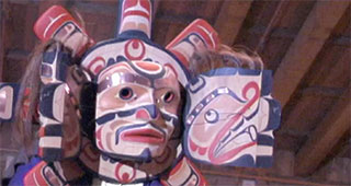 A dancer wears a brightly decorated and detailed transformation mask in the open position.