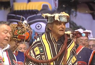 Chief Cranmer wears a ceremonial frontlet, cedar bark ring and a Chilkat blanket amidst a group of potlatchers all in regalia.