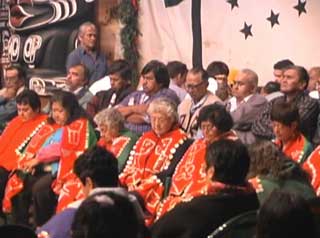 Image d’un groupe de Kwakwaka’wakw prenant part à une cérémonie de deuil au cours d’un potlatch, des anciennes portant des couvertures à boutons au premier rang.