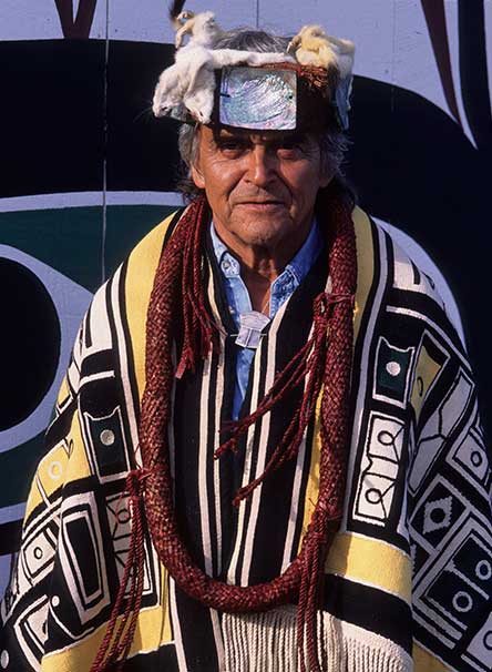 Chief Cranmer appears wearing a Chilkat blanket, cedar neck rings, a frontlet with ermine trim and mother of pearl decoration.