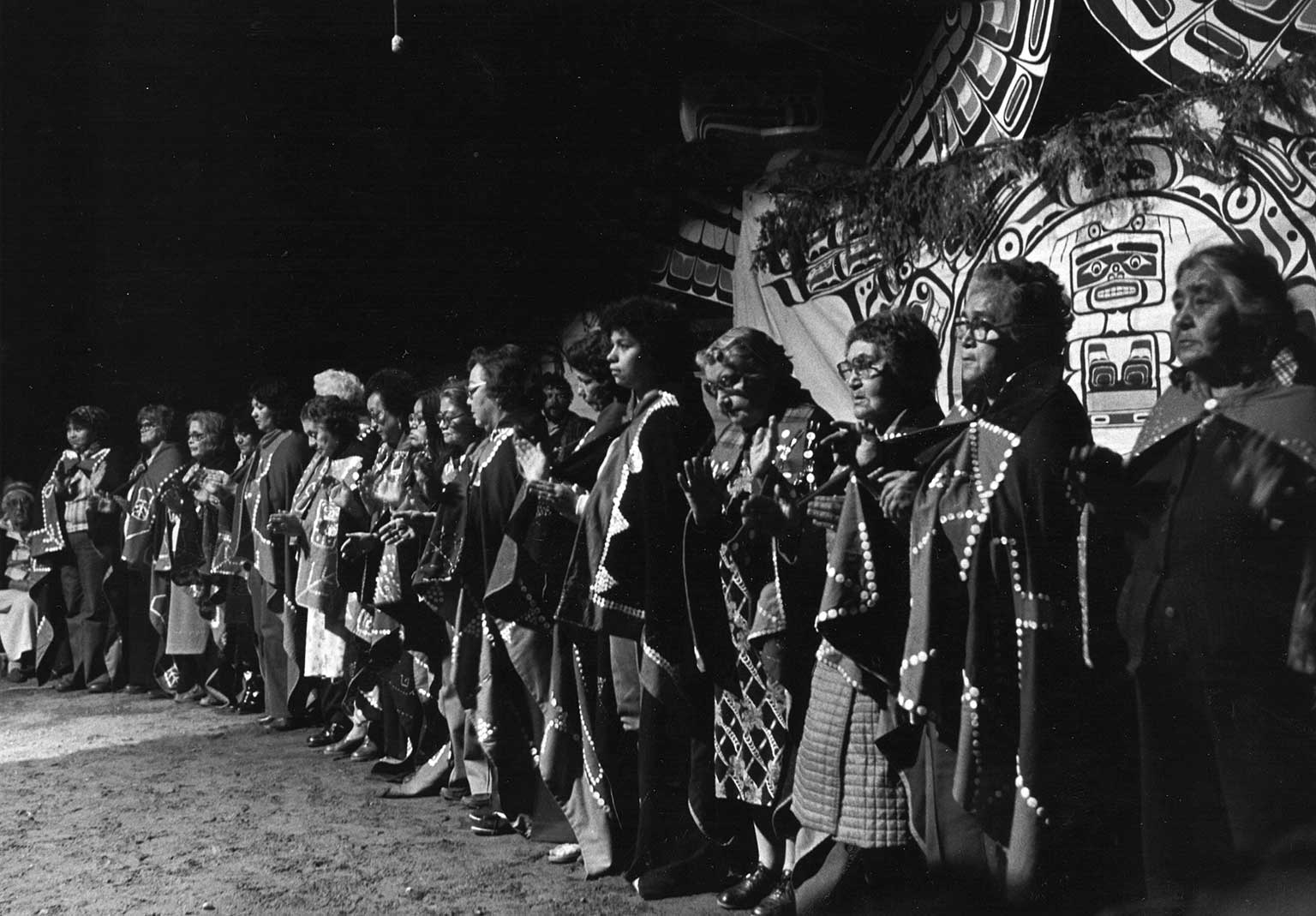 Black and white photograph of mourners in ceremonial regalia at a potlatch