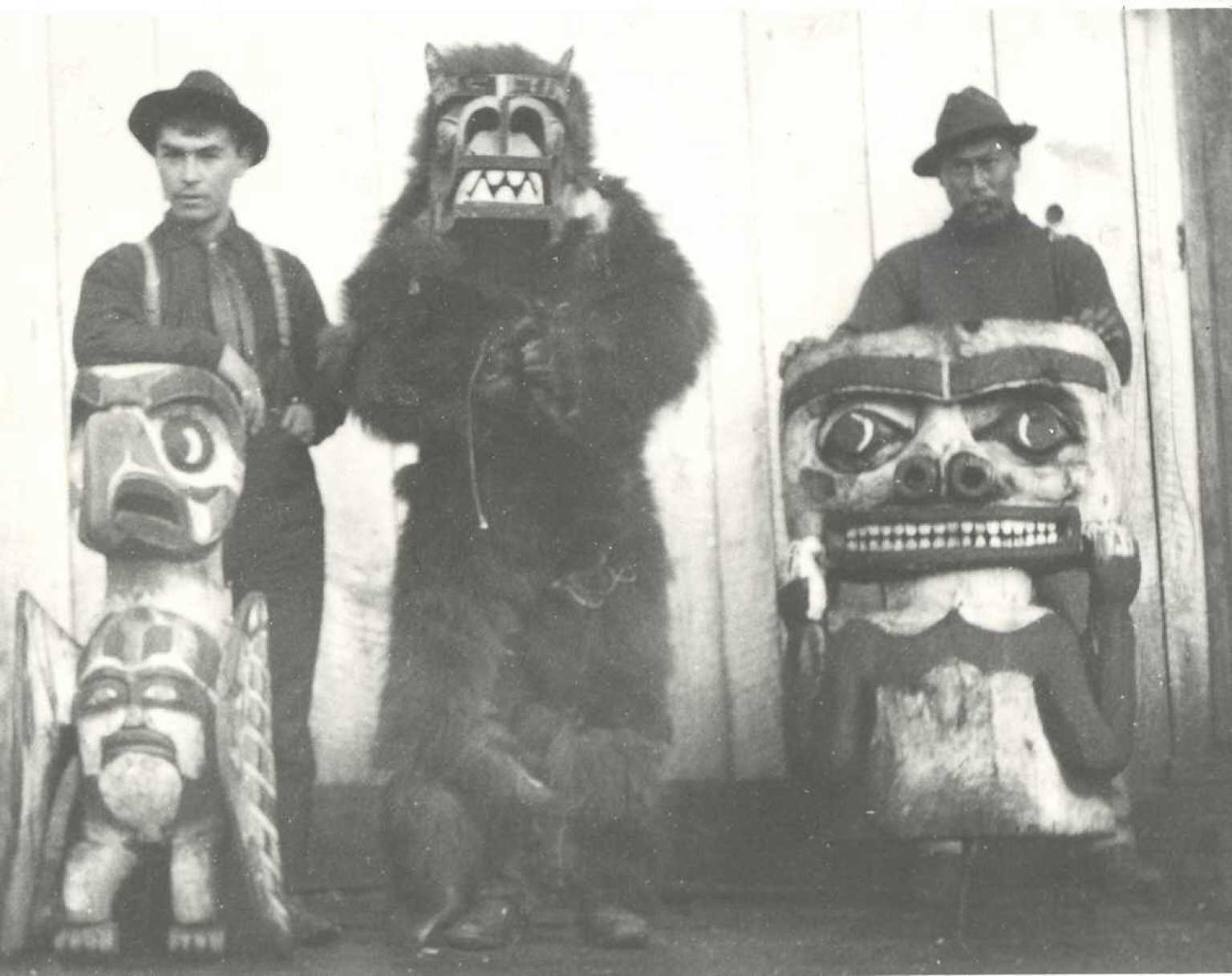 Black and white photograph of Willie Harris on left, grizzly bear dancer standing center and Naxak on right