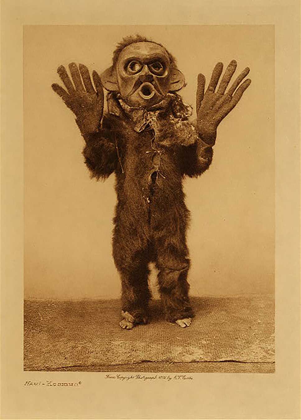 Sepia tone photograph by Edward Curtis shows dancer wearing Dzunukwa mask
