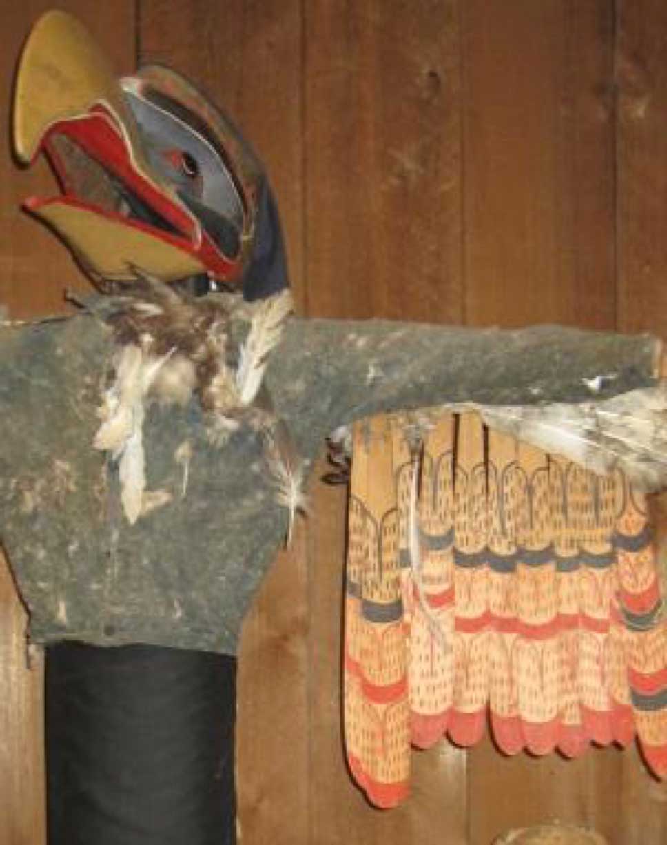 Installation photograph of Kwigwis – Sea-eagle costume shot against a cedar background
