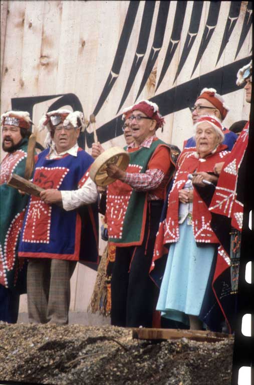 Hommes et femmes en tenue cérémonielle chantent et jouent du tambour devant le Centre culturel U'mista.