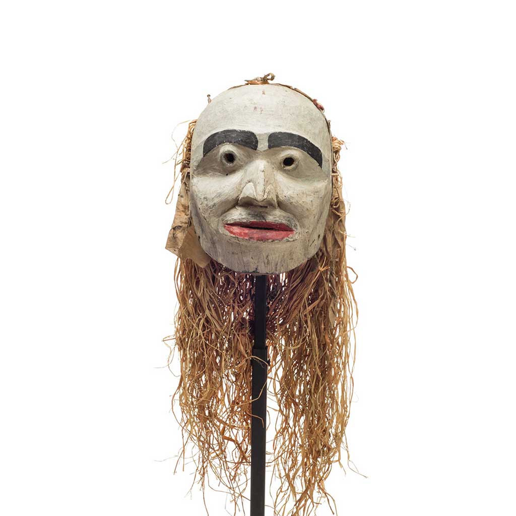 Forest spirit mask, humanoid features, mostly white face with red lips and prominent black eyebrows, cloth and cedar drape on back.