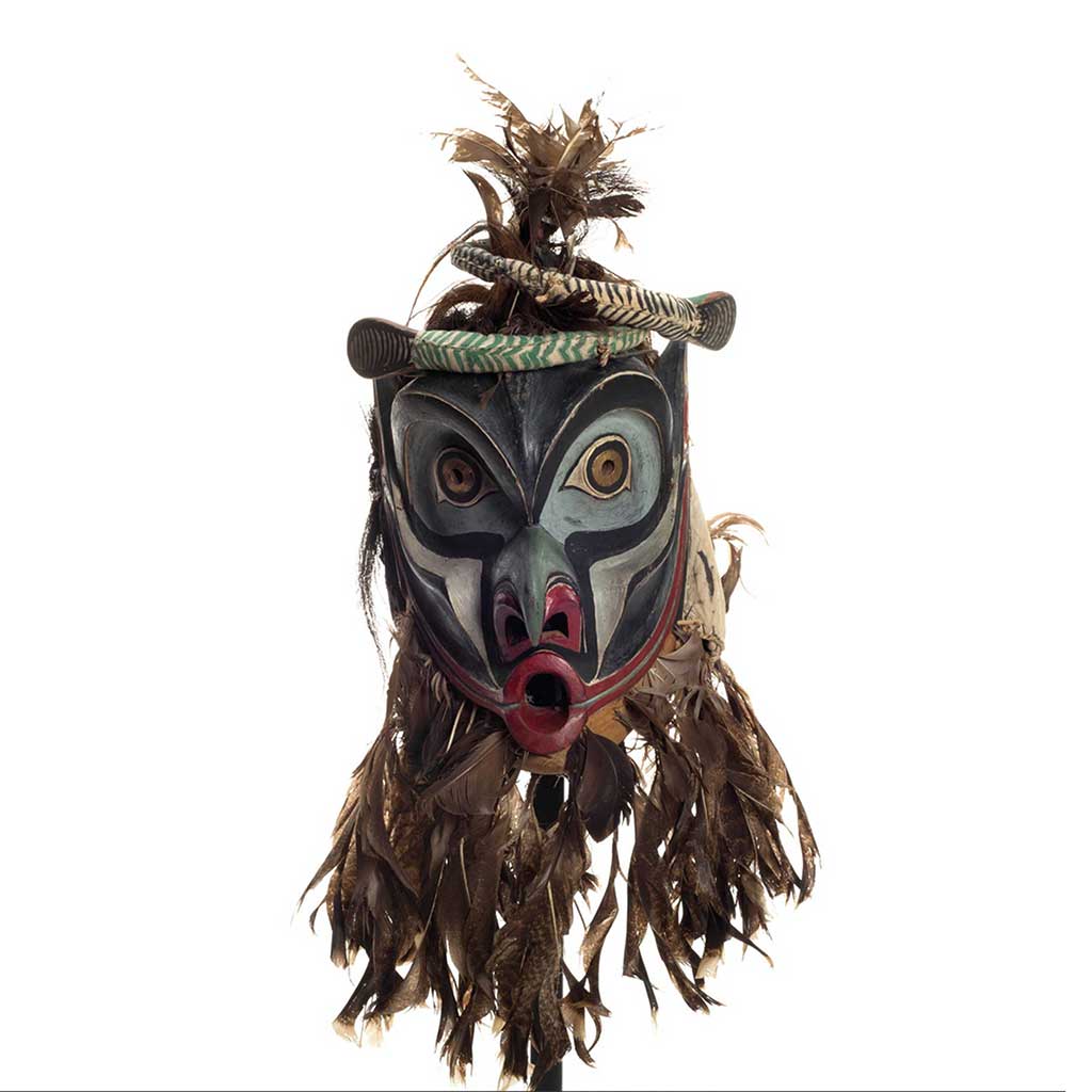 Bakwas mask with two coiled snakes atop highly arched eyebrows, brass disks with perforated centres for eyes, a beak-like nose, feather trim.