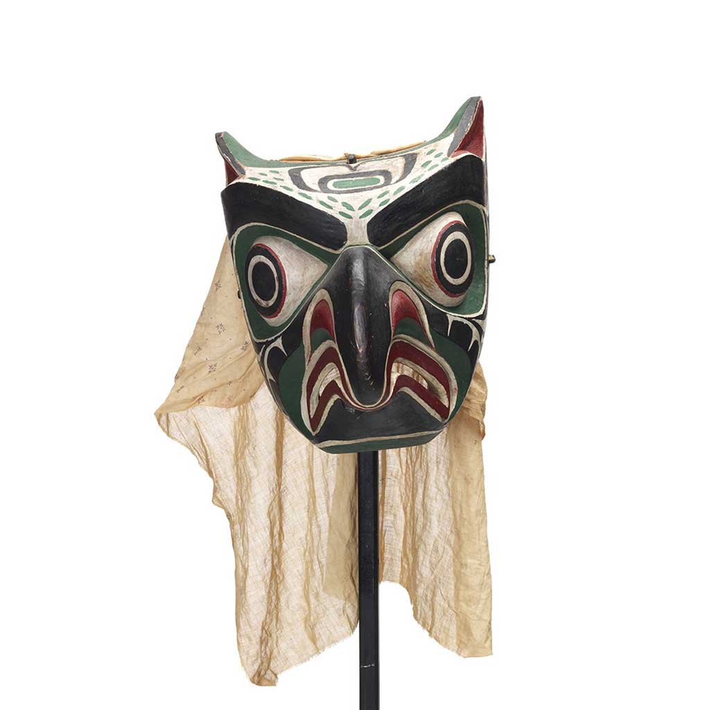Un Daxdaxalułamł, masque de hibou de couleur vive à motif noir, rouge, vert et blanc, avec un voile de coton.