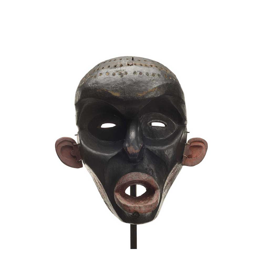Un masque d'Ogresse Dzunuḱwa, sculpture profonde, peint en noir, lèvres, joues et oreilles rouges, le crâne percé de trous pour des touffes de cheveux.