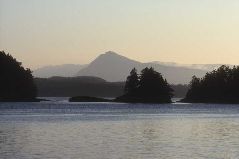 Taken near Alert Bay at sunset, image depicts ocean in the foreground, with a group of islands center and mountains in the background.