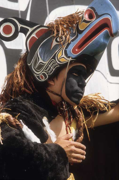 Jeune danseur au visage noirci, portant une cape de fourrure et un masque visière d'oiseau-tonnerre bordé d'écorce de cèdre.