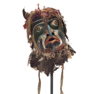D’un masque de Bakwas au nez bleu en bec crochu, des disques de laiton perforés sur les yeux ceints d’une orbite vert foncé, des marques faciales rouges, blanches et noires, un voile couvert de plumes et de poil, des rubans de couleur vive, des oreilles pointues.