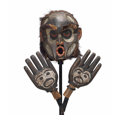 A Dzunuḱwa or wild woman of the woods mask with hands attached to mount, pursed lips painted red, mostly black with white paint details on face and hands.