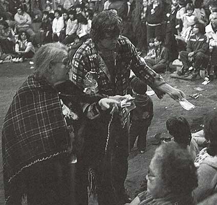 Photo noir et blanc montrant un couple (mère et fils) distribuant des dons d'argent lors un potlatch.