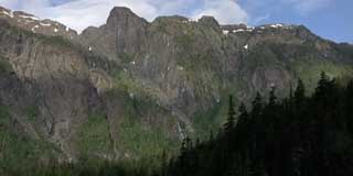 Photographie d’un massif montagneux aux pics montrant des traces de neige et avec une bande forestière au premier-plan.